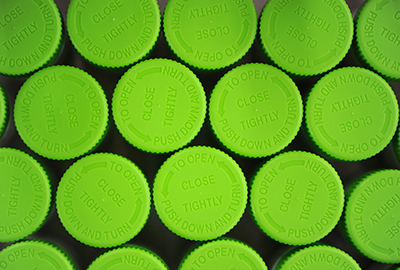 Overhead shot of green drug bottle caps which state "To Open, Push Down And Turn".